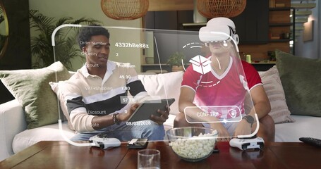 Holding tablet, two men cream-sweater and red-shirt using VR-headset on sofa at home, AR overlay