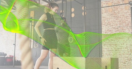 Stepping female in black sleeveless top and shorts onto plyo box at gym, with green overlay