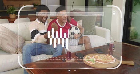 Cheering two men wearing red jersey and light-polo in living room, holding soccer ball and pizza