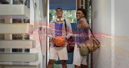 Standing two men holding basketball, carrying duffel in entryway, wearing hoodie and sleeveless top