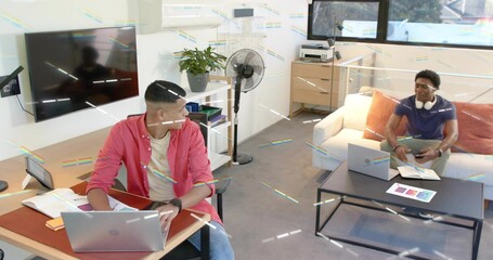 Working left-side man at desk in home office wearing button-up over tee, using laptop and papers