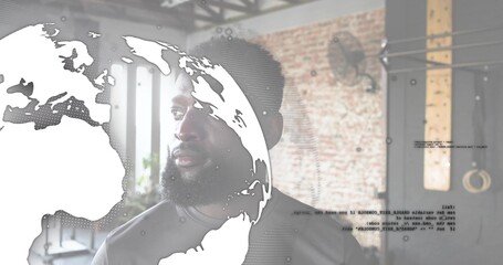 Standing man with beard wearing dark athletic T-shirt in fitness studio, globe overlay, pull-up rig