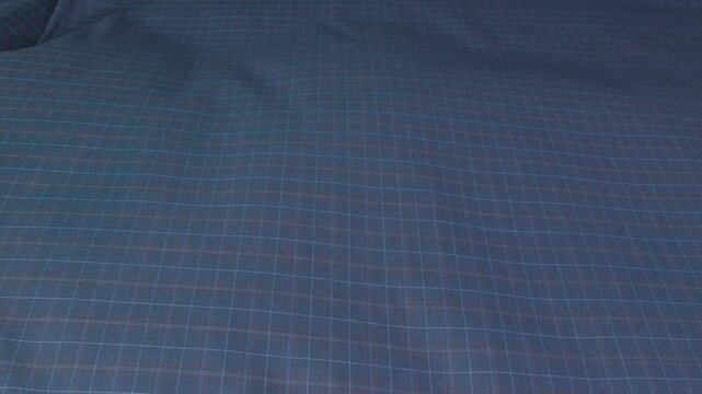 female unrolling roll of blue checkered fabric on cutting table at sewing factory