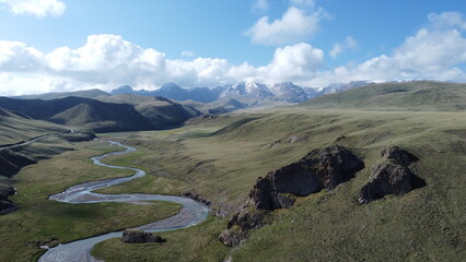 Aerial view of a winding river flowing through a green mountain valley. Remote landscape with dramatic terrain, natural patterns and untouched wilderness, photographed from a drone. © Szymon