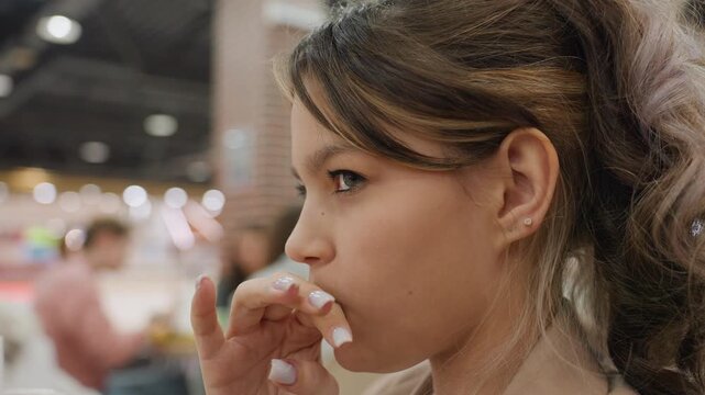teen enjoying treat in crowded mall, caucasian teenager sampling sweet snack amid bustling mall environment, casual scene of young person tasting dessert at shopping mall food court