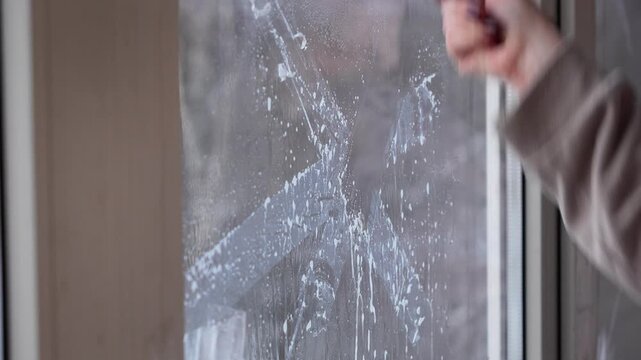 woman cleans dirty window from glue from old scotch tape with a special tool with a blade. cleaning, tidying up, washing windows. window protection against shock wave