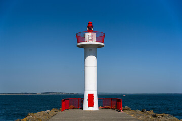 View of a striking red and white lighthouse standing tall against the vast expanse of the deep blue sea and clear sky in Howth, Dublin, Ireland.