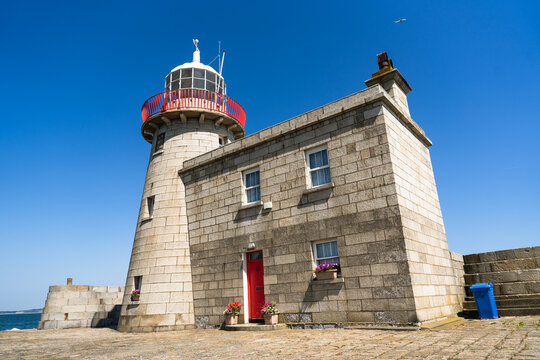 View of a majestic stone lighthouse with a striking red door stands proudly against the clear blue sky, a beacon of maritime history, Howth, Dublin, Ireland.
