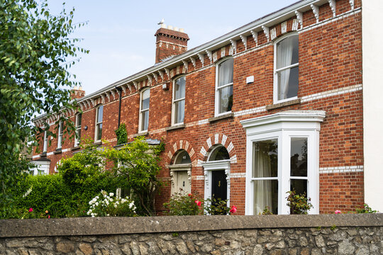View of red brick houses stand proudly behind a stone wall, adorned with blooming flowers and lush greenery, a picturesque scene, Dalkey, Dublin, Ireland.