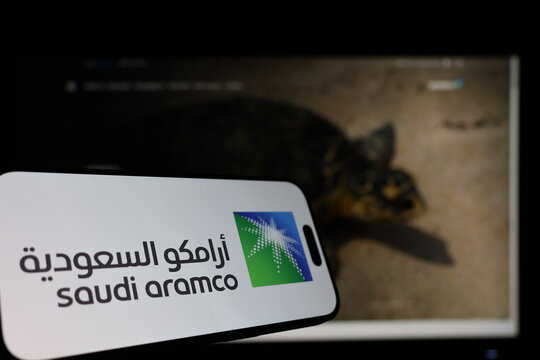Kiel, Germany - 01-12-2026: Smartphone displaying Saudi Aramco logo in front of the company website on a monitor
