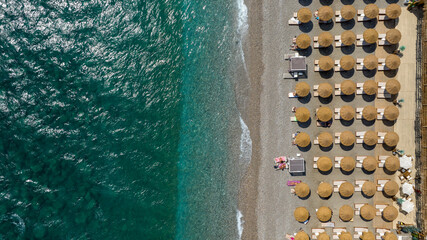 Top-down aerial view of a pebble beach, featuring a dense, organized grid of golden straw parasols....