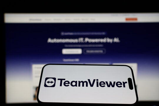Kiel, Germany - 01-12-2026: Smartphone displaying TeamViewer logo in front of the company website on a monitor