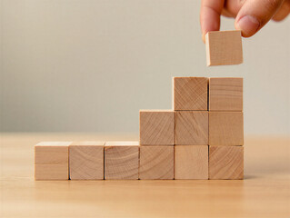 A person building a pyramid with wooden blocks on a table in a room with a light colored wall and floor