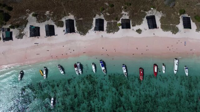 Stunning high-angle drone shot capturing the iconic pink sand beach of Padar Island in Komodo National Park, Indonesia. A narrow strip of soft pink-white sand curves between lush green volcanic hills 