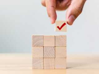 Hand holding wooden block with red checkmark above stack of blocks on table