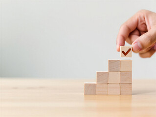 Hand placing wooden block with checkmark on top of stacked blocks on a table