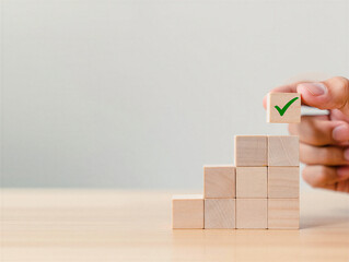 Wooden blocks stacked in a pyramid shape with a hand placing a green checkmark block on top  business concept