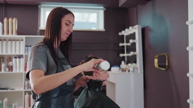 caucasian colorist carefully measuring and dosing hair product into bowl, side view in stylish salon, precise hands and labeled bottle, professional shelves and mirrored vanity in background
