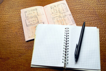 Empty grid notebook open beside a passport filled with border crossing stamps. Symbolizes fresh start documentation, visa application preparation, relocation planning ritual, and nomad essentials.
