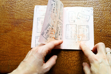 Female hand flipping stamped passport pages with many border stamps. Symbolizes life under paperwork, cross border uncertainty, identity within global systems, and the human side of modern migration.