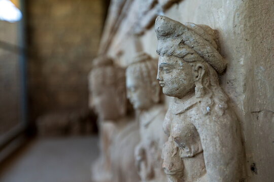 View of weathered stone sculptures depicting serene figures with intricate headdresses and delicate features, showcasing ancient artistry, Taxila, Khyber Pakhtunkhwa, Pakistan.