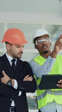 Attractive successful stylish bearded manager standing with purposeful experienced african american builder or engineer on construction site indoors and both are happy to achieve a good result in