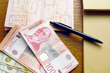 Serbian dinar banknotes scattered near stamped passport and blank notepad. Represents migration preparation, multi jurisdiction living, paperwork survival essentials, and life admin under instability.