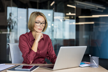 Professional businesswoman with glasses thinking while concentrating on her work, using a laptop at...