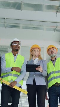 Likable smart stylish bearded man and blond woman-main managers of building company discussing building project with professional executive mixed races builders when walking on construction site