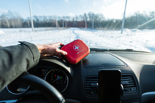 Driver Checking Red First Aid Kit On Dashboard At Snowy Roadside, Hands Inspecting Clasp And Compact Interior, Smartphone Mounted, Daylight Clarity, Proactive Safety Routine