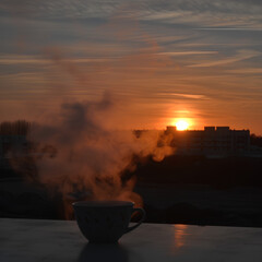 Steam rising from a ceramic teacup near a window, blurred cityscape behind.