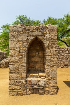 View of weathered stone niche standing against the test of time, framed by the soft green of distant trees, and bathed in the warm glow, Taxila, Punjab, Pakistan.