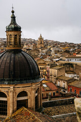 Panoramic View Over Ragusa From Cathedral Of San Giovanni Battista: Historic Sicilian City Rooftops, Church Domes, And Dense Stone Architecture Under Overcast Sky