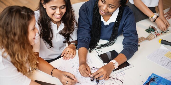 Three young women collaborating on a tech project. Diverse group of students working on electronics. Teamwork and innovation in a classroom setting. Young diverse students learning together in library