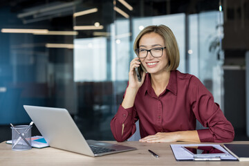 Smiling businesswoman talking on mobile phone at her desk, managing communication and business...