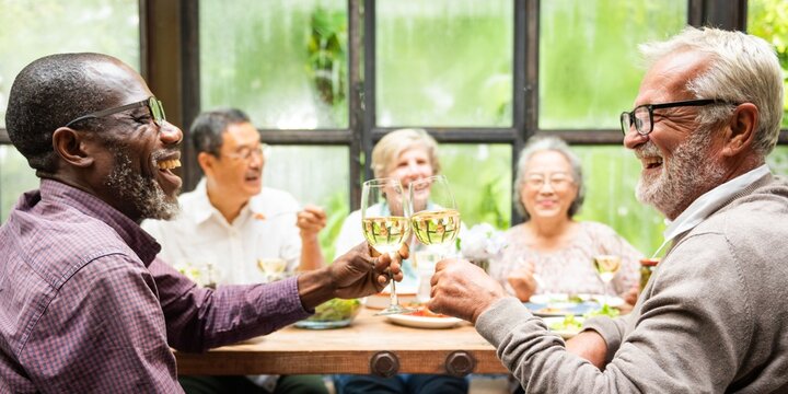 Group of diverse seniors enjoying a meal, laughing and toasting with wine glasses. Elderly friends, happy gathering, cheerful seniors at a dining table. Diverse senior people drinking wine at lunch.
