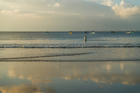 View of gentle waves kissing the shore, mirroring the soft sky above with distant boats dotting the horizon, a serene escape, Kuta Beach, Bali, Indonesia.