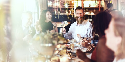 Group of people enjoying a lively dinner party, laughing and toasting. Warm atmosphere with diverse guests, sharing joy and conversation at a festive gathering. Friends celebrating at dinner.