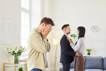 Sad man covers face while couple embraces in background, creating emotional scene of jealousy and...