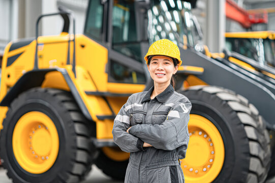 A confident worker in a safety helmet stands proudly in front of heavy machinery, showcasing a blend of professionalism and industry.