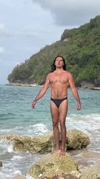 Freediver Celebrating Triumph, Athletic Man On Seaside Cliff, Energetic Male Freediver Poses On Rocky Shoreline, Dynamic Underwater Enthusiast Displays Strength Amid Ocean Spray And Cloudy Sky