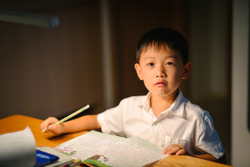 Seven-year-old Asian boy focused on doing homework and writing at a desk in a cozy home setting
