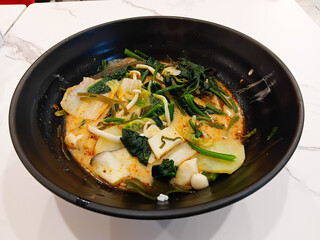 Spicy mala soup served in a black bowl, filled with vegetables and herbs, rich chili broth, hot flavor, Asian comfort food style.