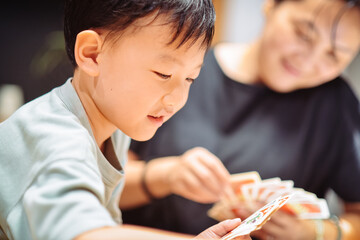 Asian mother and seven-year-old son playing card games together in a cozy home indoor setting