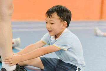 Seven-year-old Asian boy doing warm-up exercises on an indoor badminton court