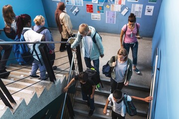 Students of diverse ethnicities, including males and females, walk up and down stairs in a school. Backpacks and casual attire are visible in the busy hallway. Students and education concept. © Rawpixel.com