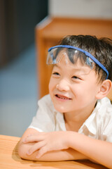 Happy seven-year-old Asian boy wearing blue safety goggles and laughing during a home science experiment