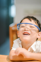 Happy seven-year-old Asian boy wearing blue safety goggles and laughing during a home science experiment