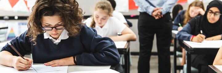 Focused students in a classroom writing and taking an exam. Diverse students in uniforms taking exam. Classroom exam setting with attentive students and teacher. Teacher look out students taking exam © Rawpixel.com