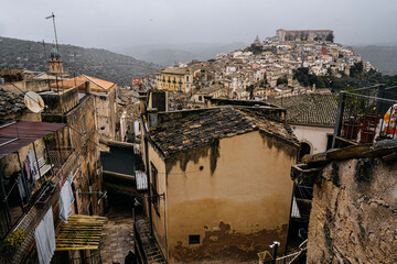 Hilltop City Of Ragusa In Sicily Under Overcast Sky: Historic Stone Buildings And Dense Urban Landscape In Soft Diffused Light And Hazy Weather